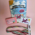 Cross stitch luggage tag kit with materials on a pink background