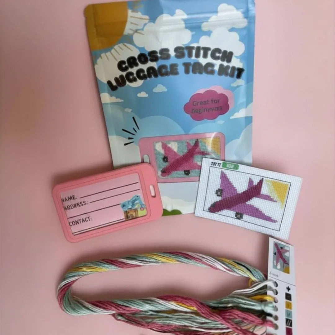 Cross stitch luggage tag kit with materials on a pink background