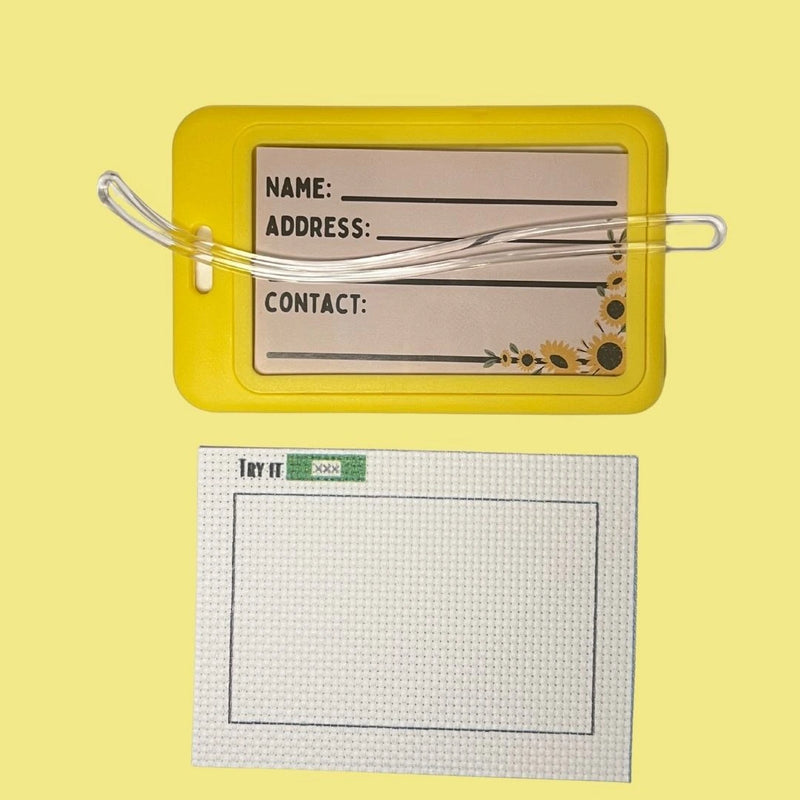 Yellow luggage tag with clear strap and address label on a yellow background with 14ct AIDA fabric
