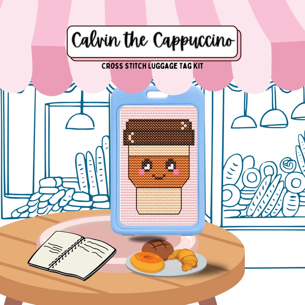 Cross stitch luggage tag kit for 'Calvin the Cappuccino' with a coffee-themed design on a table with a plate of pastries.