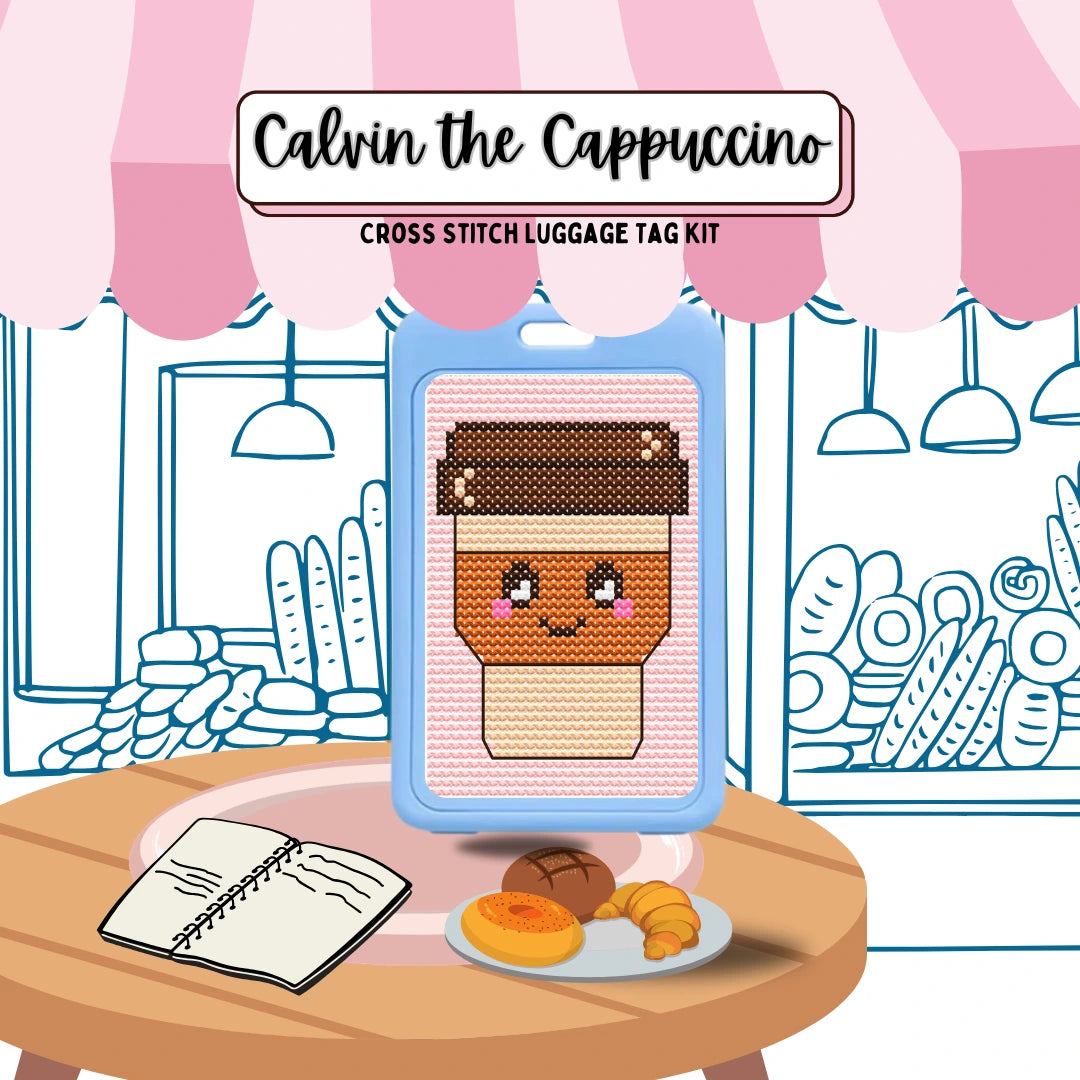 Cross stitch luggage tag kit for 'Calvin the Cappuccino' with a coffee-themed design on a table with a plate of pastries.