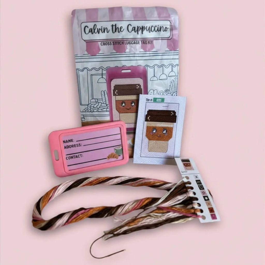Calvin the Cappuccino cross stitch luggage tag kit with materials on a pink background
