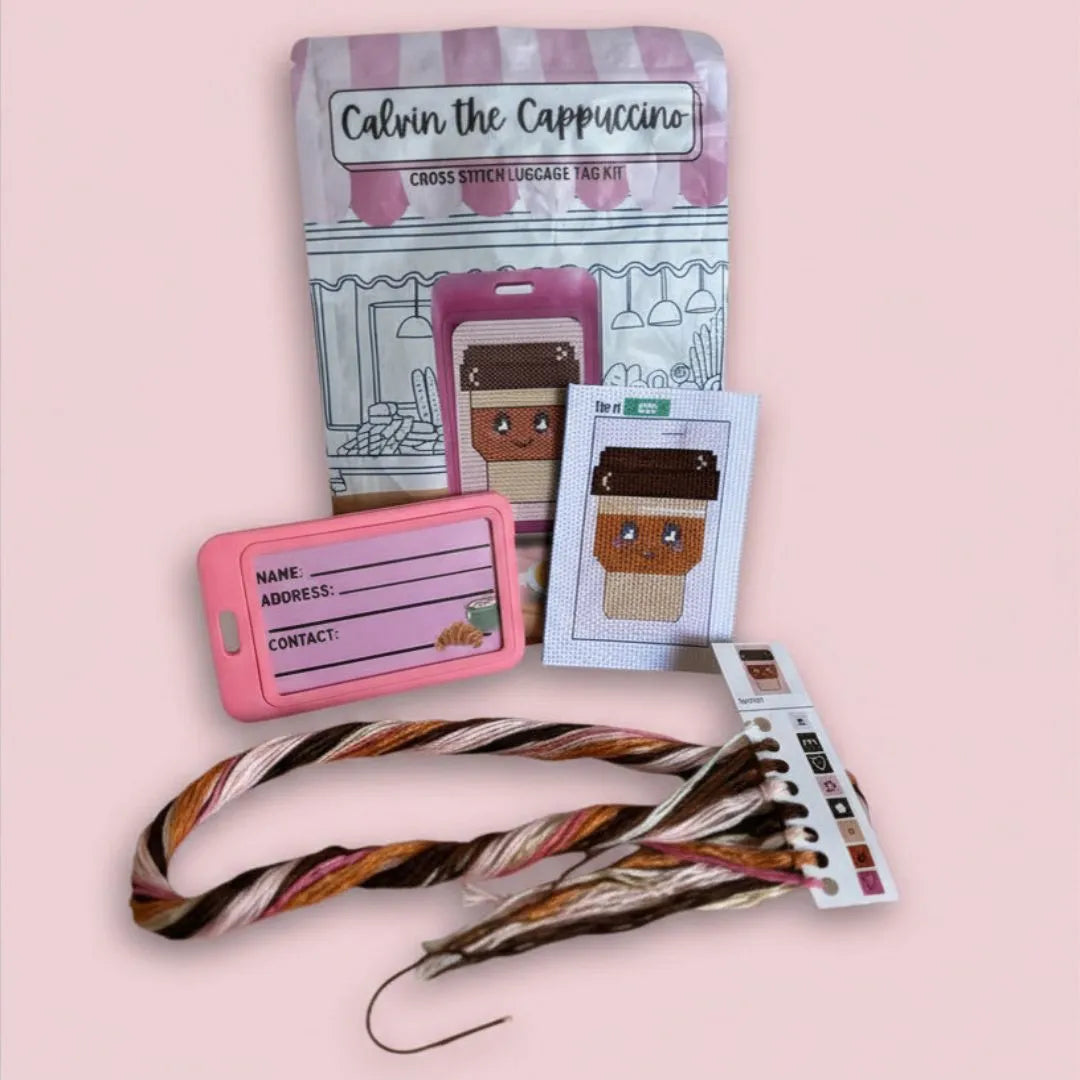 Calvin the Cappuccino cross stitch luggage tag kit with materials on a pink background