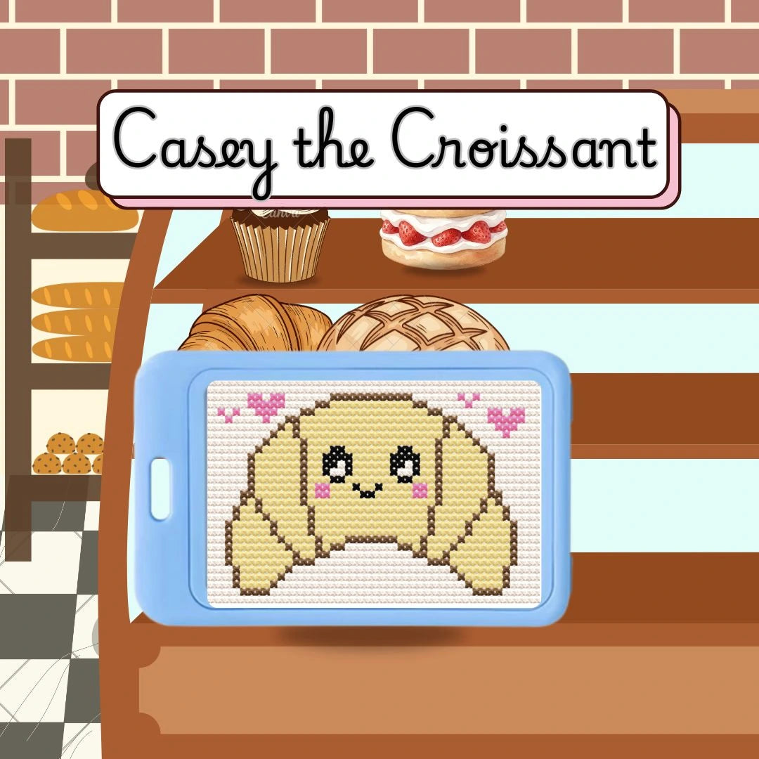 Cross-stitched design of a croissant on a tablet with a bakery background, featuring 'Casey the Croissant'.