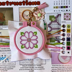 Cross-stitched keychain with pink hoop and floral design, surrounded by crafting materials and instructions.