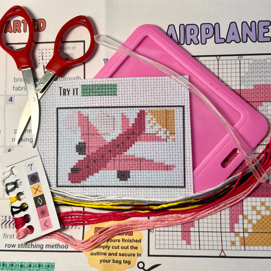 Pink Airplane cross stitch DIY luggage tag kit with a pink bag tag, luggage tag attachment, Scissors, needle and thread, stamped Aida fabric, color instructions