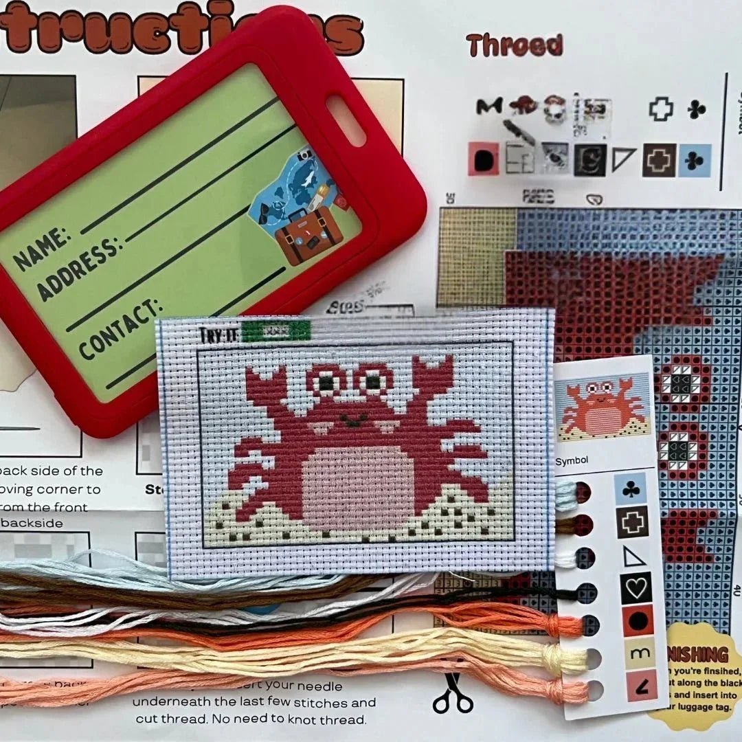 Cross-stitch kit with a crab pattern, threads, and instructions on a white background